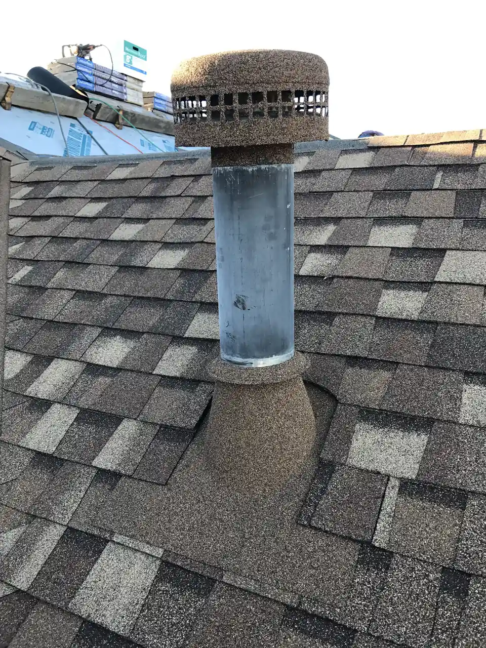 The same water heater vent pipe before coating: bare galvanized metal on the new gray shingle roof