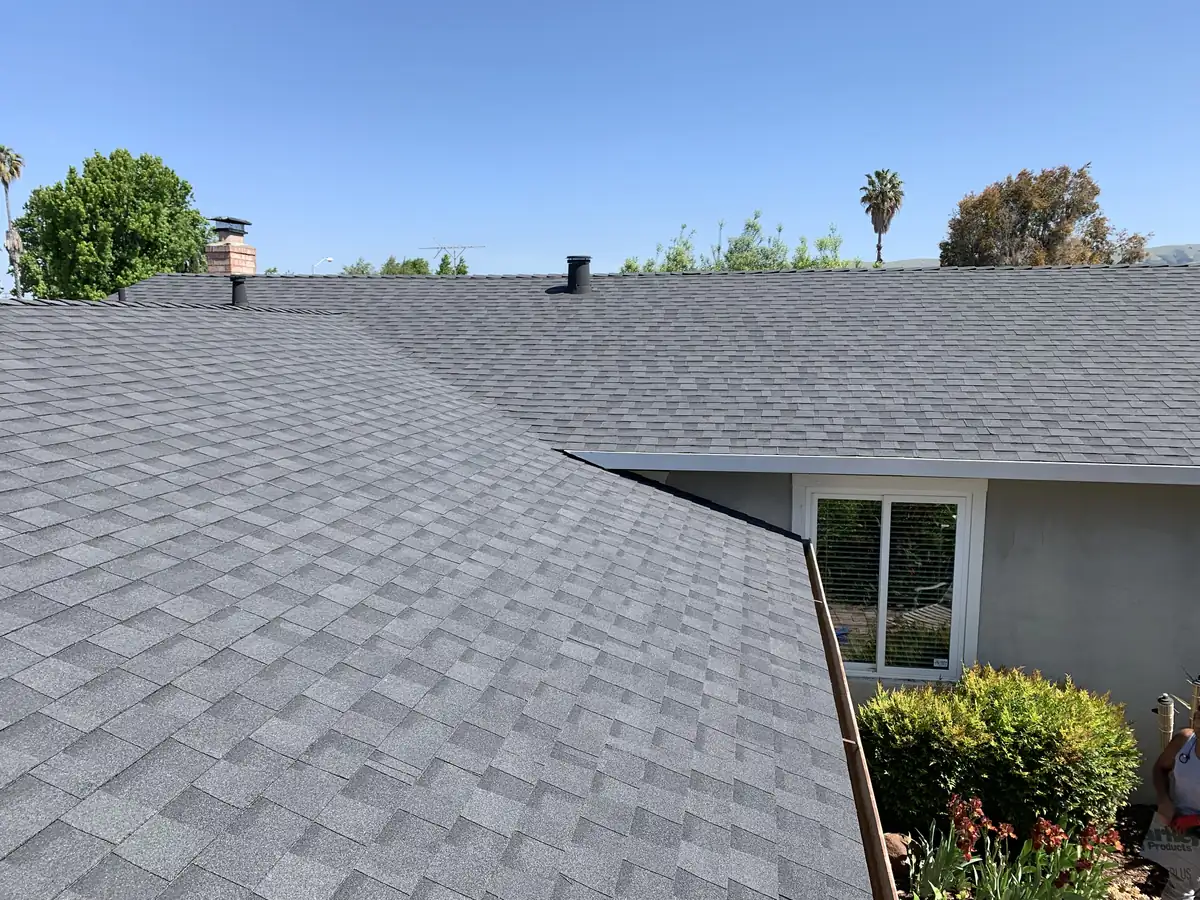New light gray shingle roof over a single-story house with a stone-coated pipe near the ridge, palms and hills behind