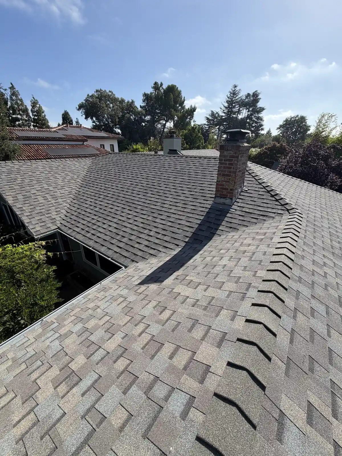 Gray shingle roof with a brick chimney, stone-coated valley and hip, a neighboring tile roof visible